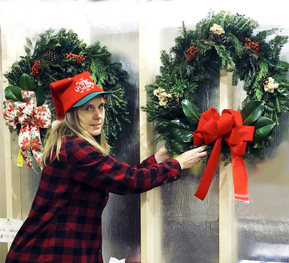 A woman in a plaid shirt is hanging a christmas wreath on a wall.