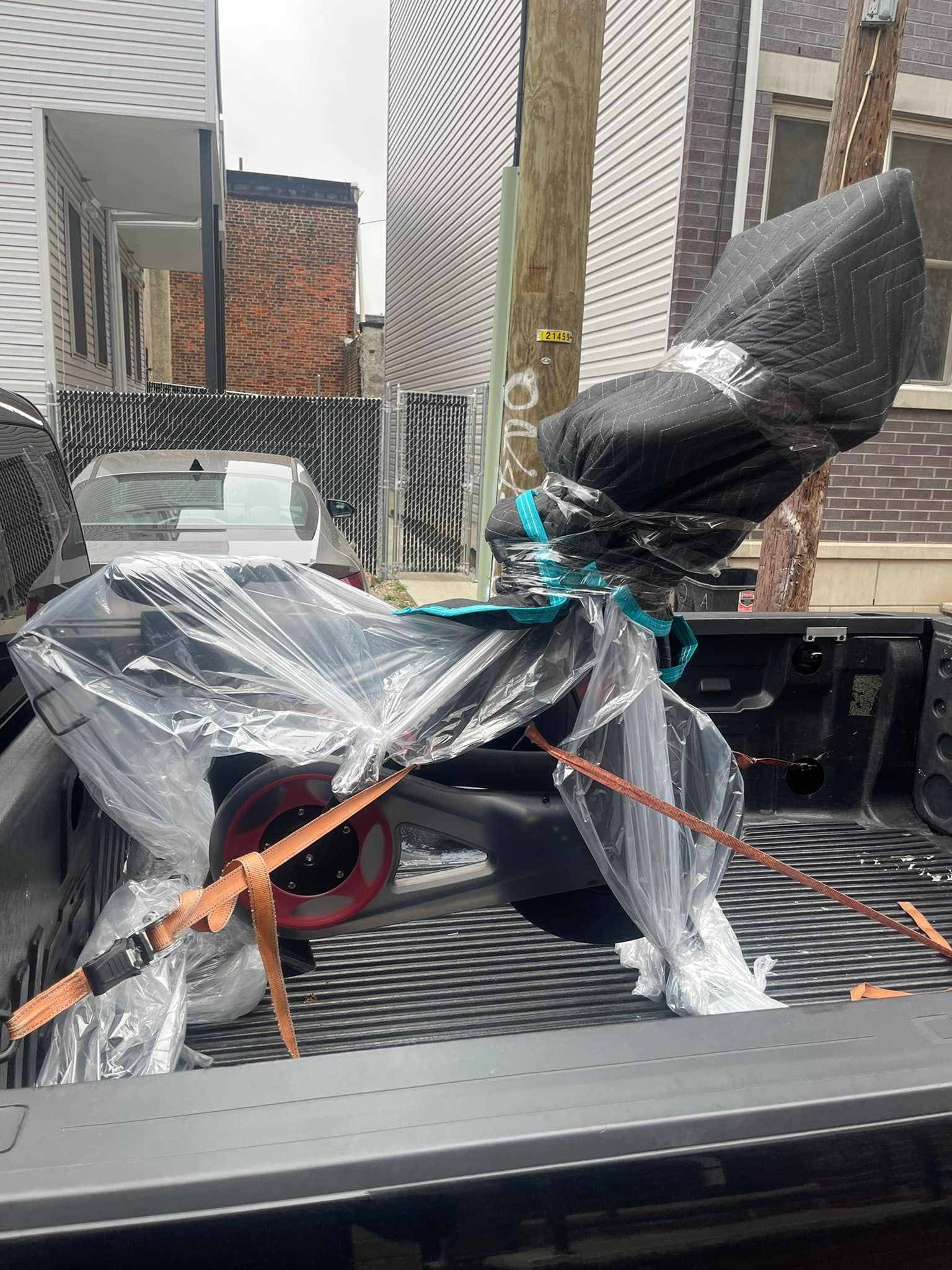 A wrapped exercise machine secured in a truck bed, with buildings in the background.