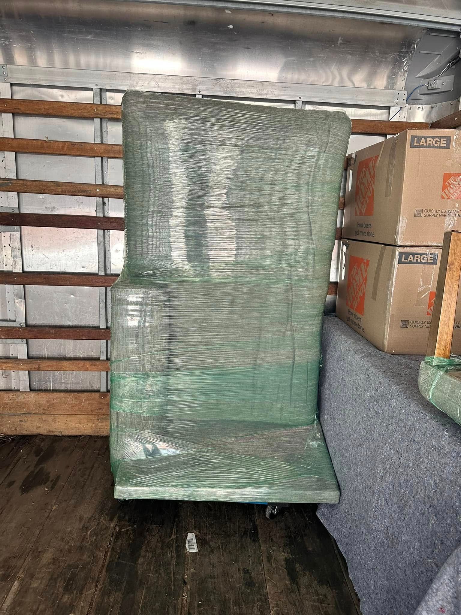 A chair wrapped in green plastic wrap inside a moving truck, boxes in the background.