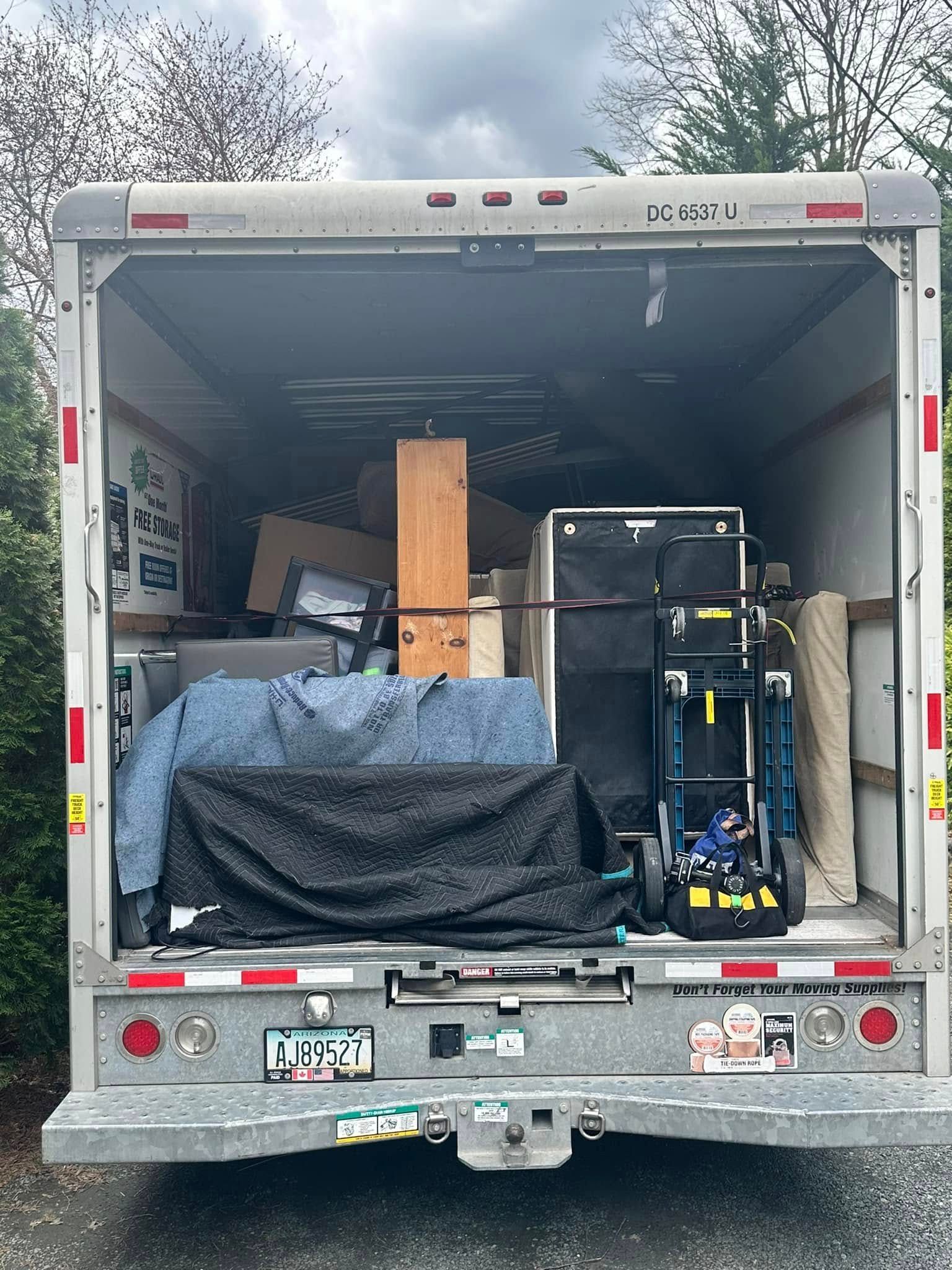 Open back of a moving truck filled with furniture and boxes; outdoors, daylight.