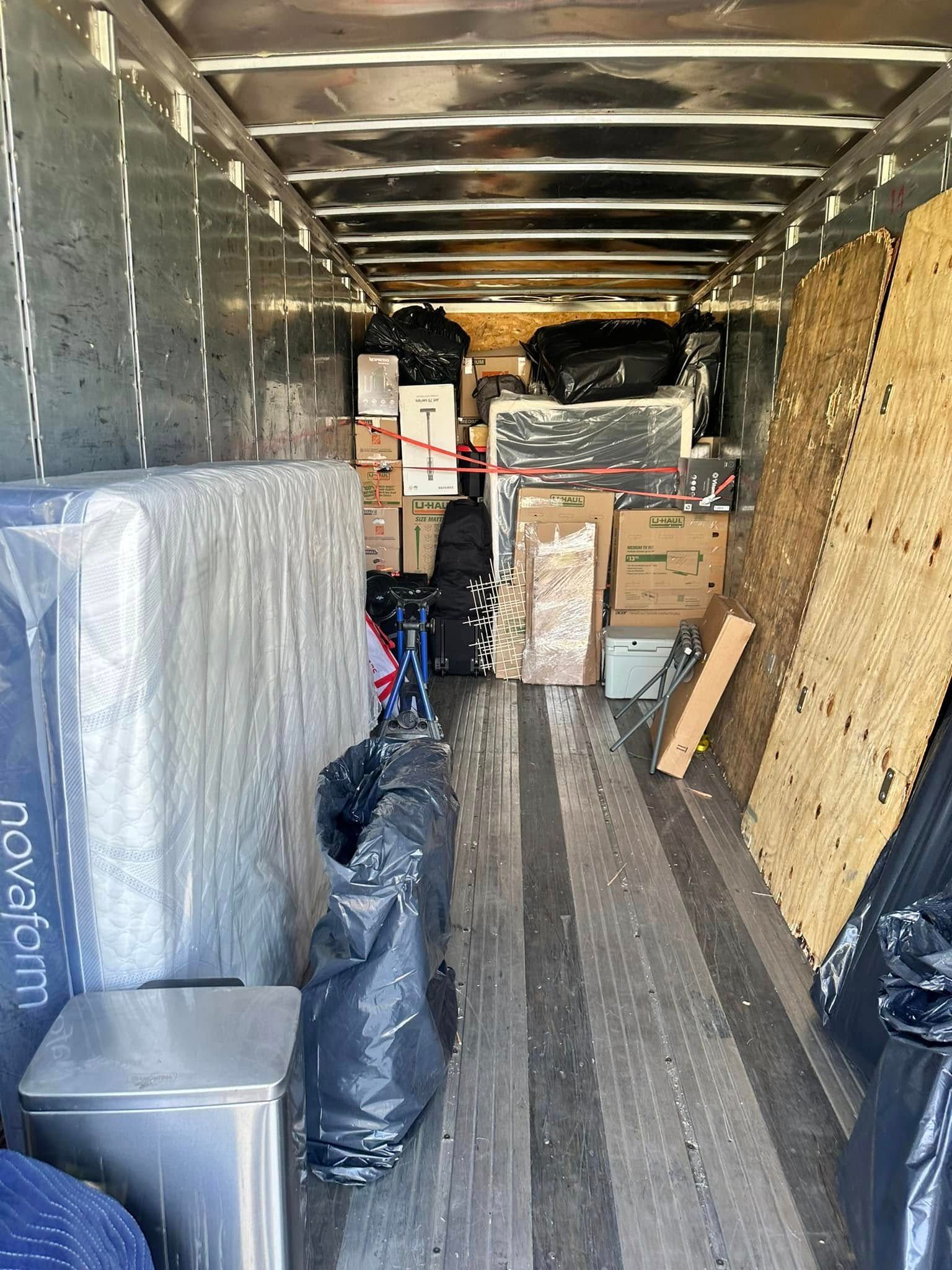 Inside of a packed moving truck: boxes, wrapped mattress, trash bags, and other household items.