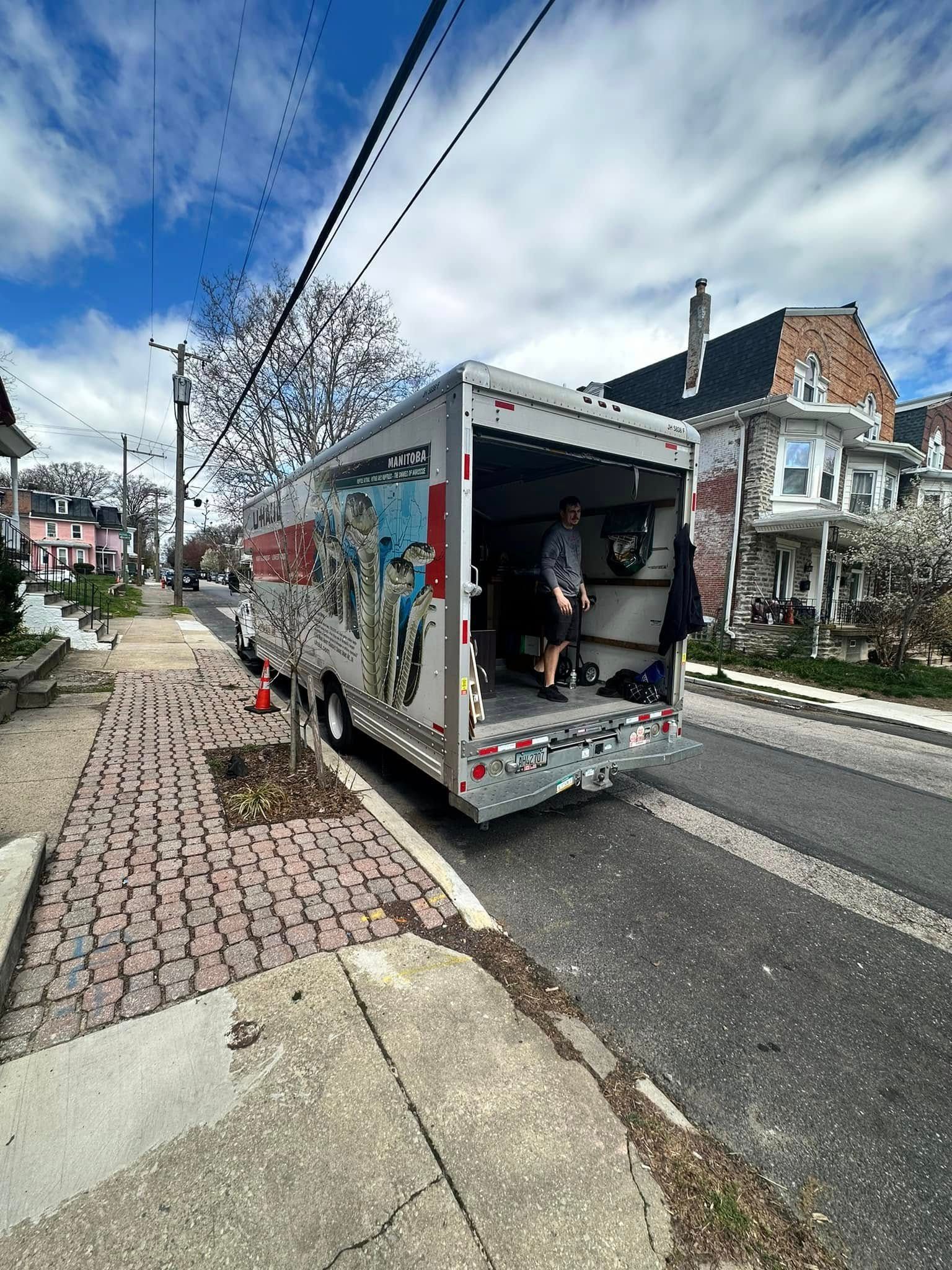 A person is inside a parked silver trailer on a city street. The trailer's door is open. Brick sidewalk.