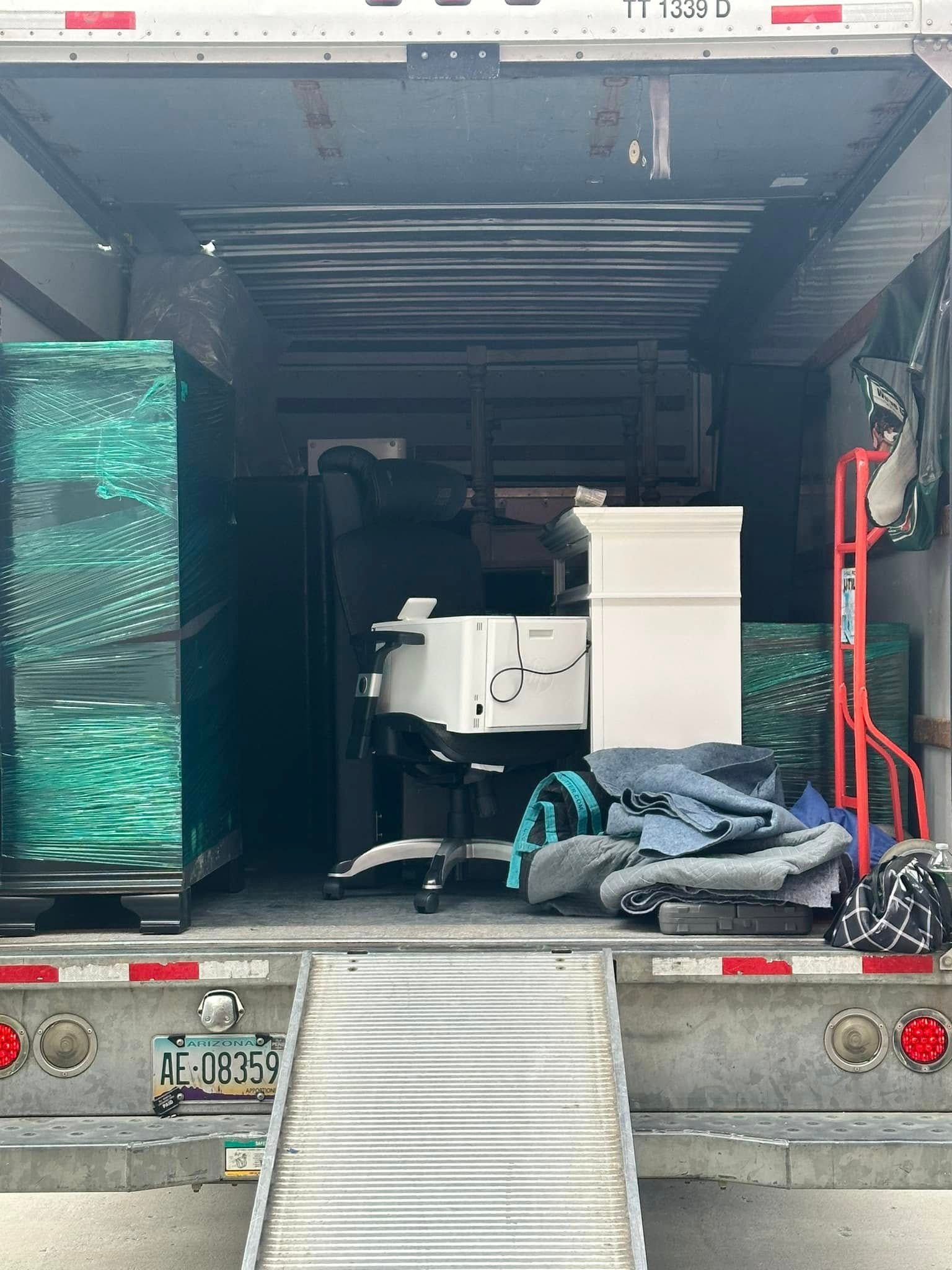 Inside of moving truck filled with furniture and boxes. Ramp down, green and black cabinets, white boxes.