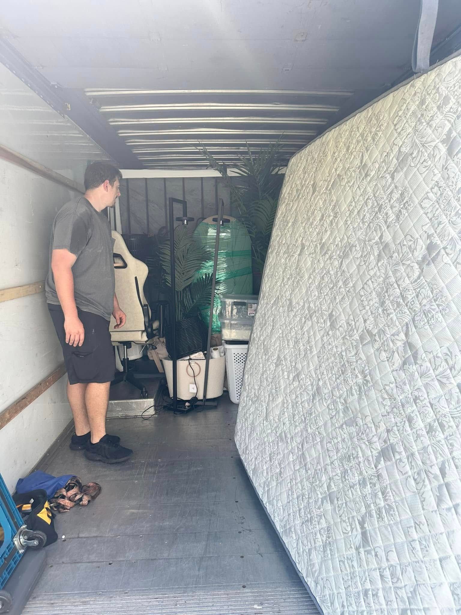 Person loading items into a truck. A mattress is propped up. Boxes and other items are inside.