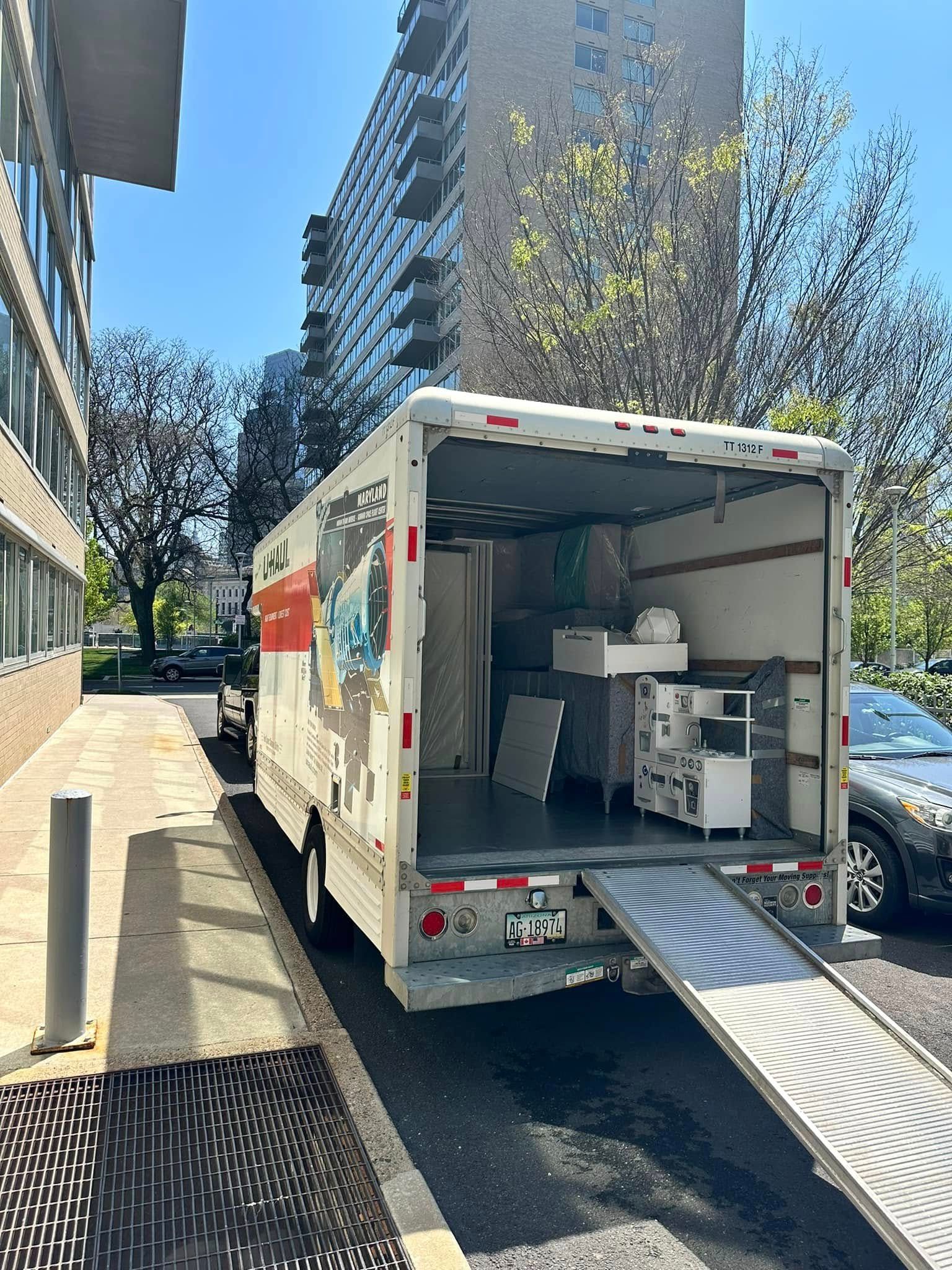 Moving truck with ramp open; parked near building. Contents visible inside.