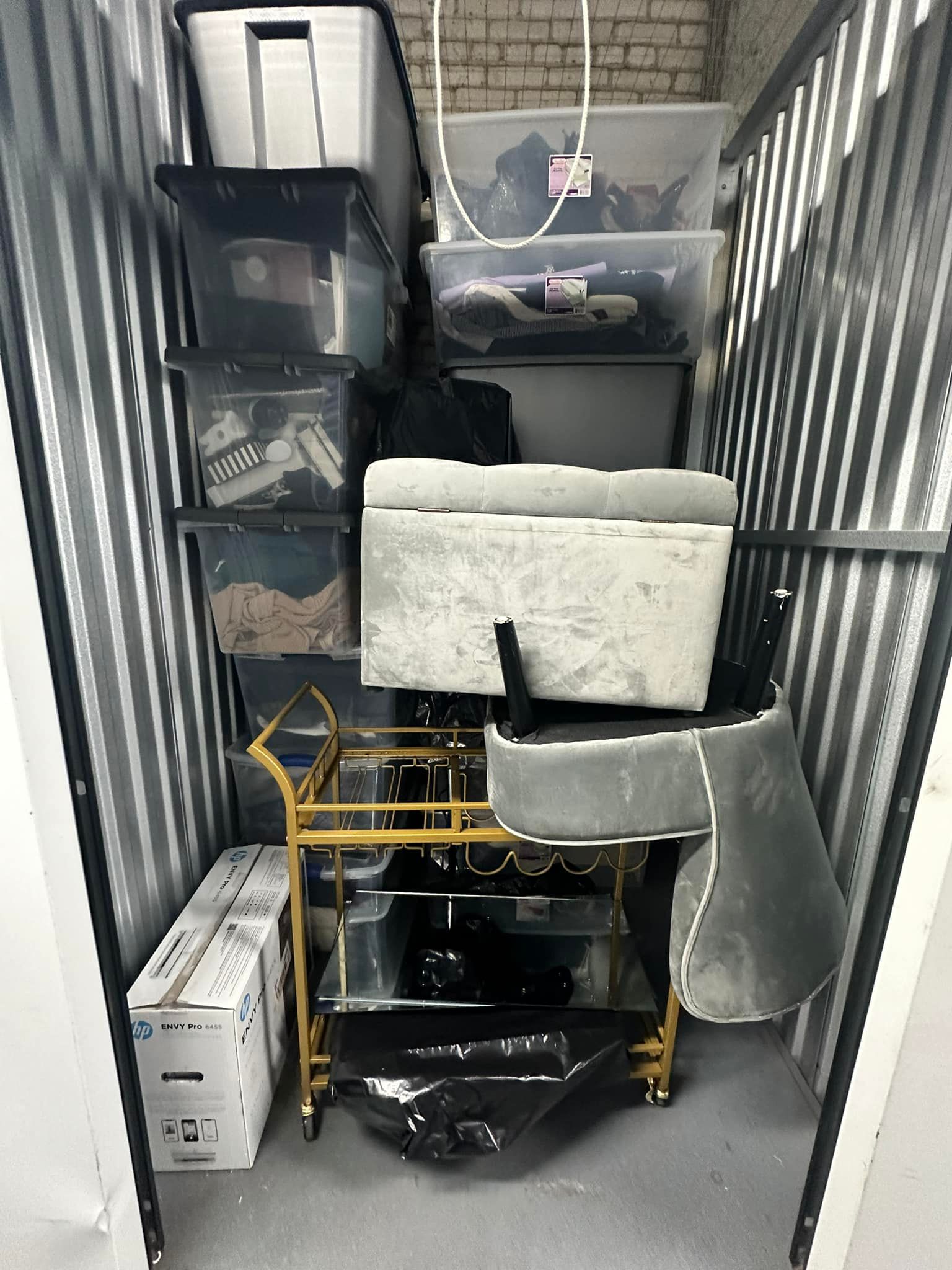 Storage unit packed with boxes, furniture, and a bar cart. Black, white, and gold items.