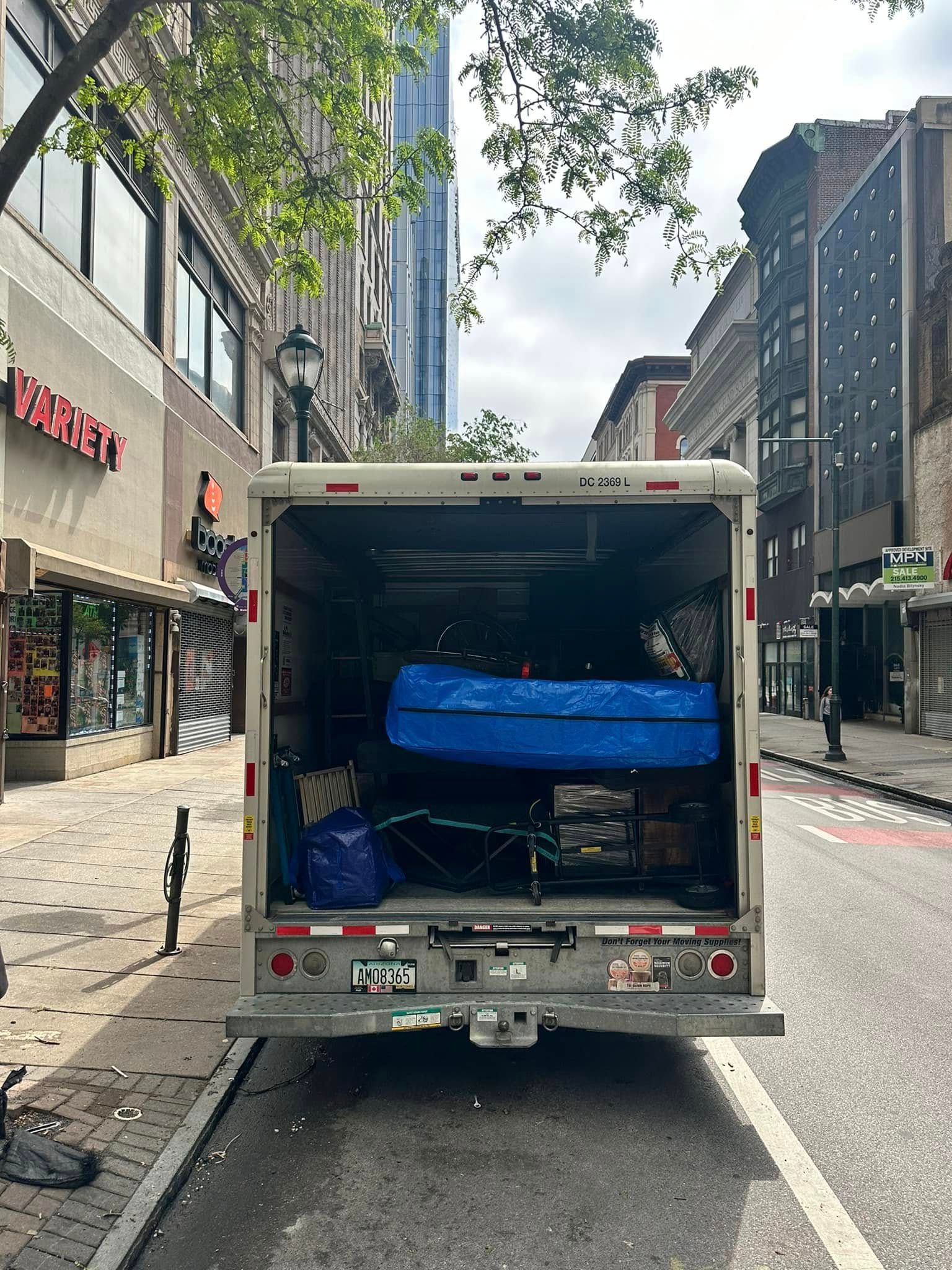 Back of a moving truck parked on a city street, loaded with furniture and items.