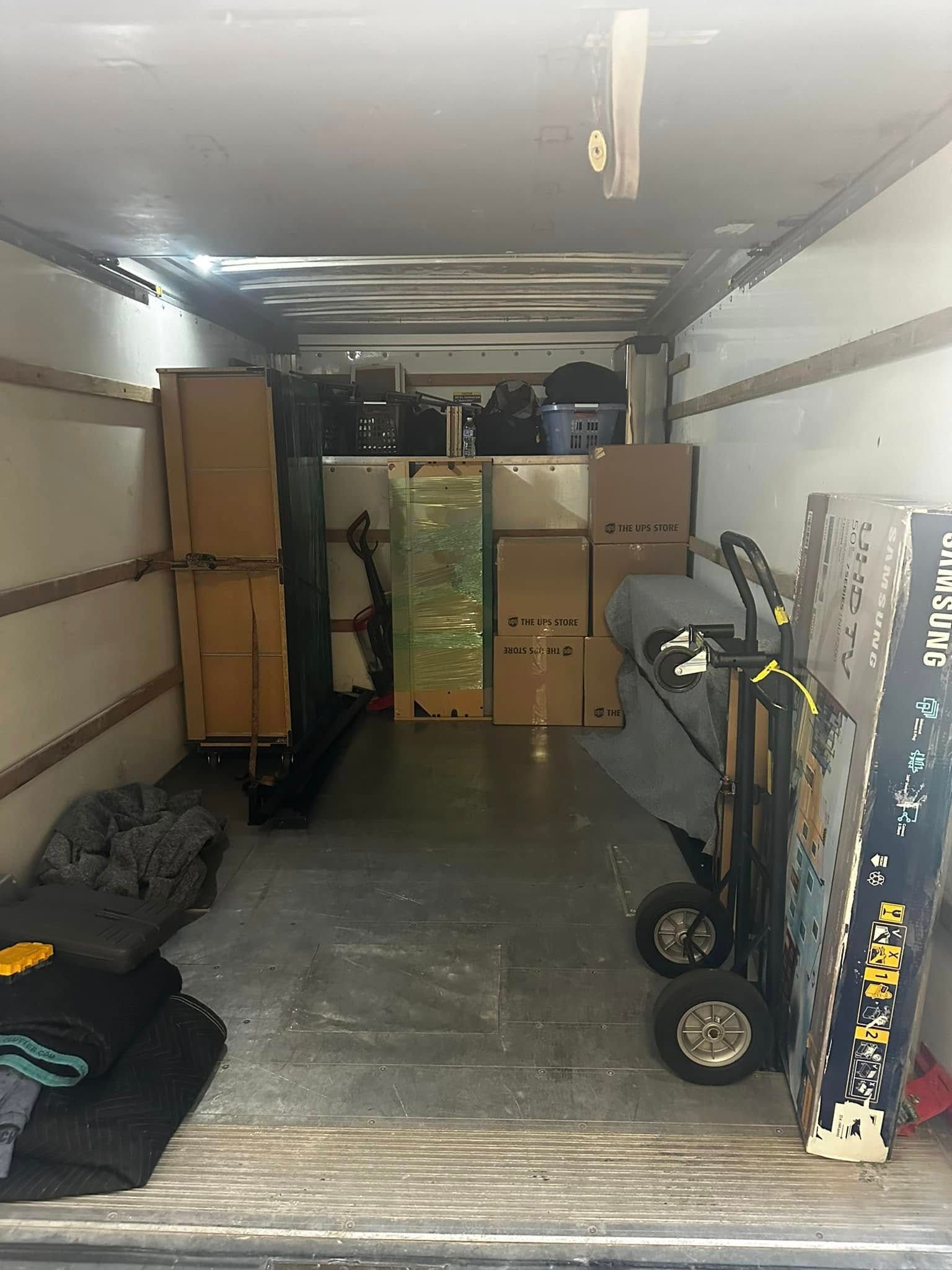Interior of a moving truck packed with cardboard boxes, furniture, and a hand truck.