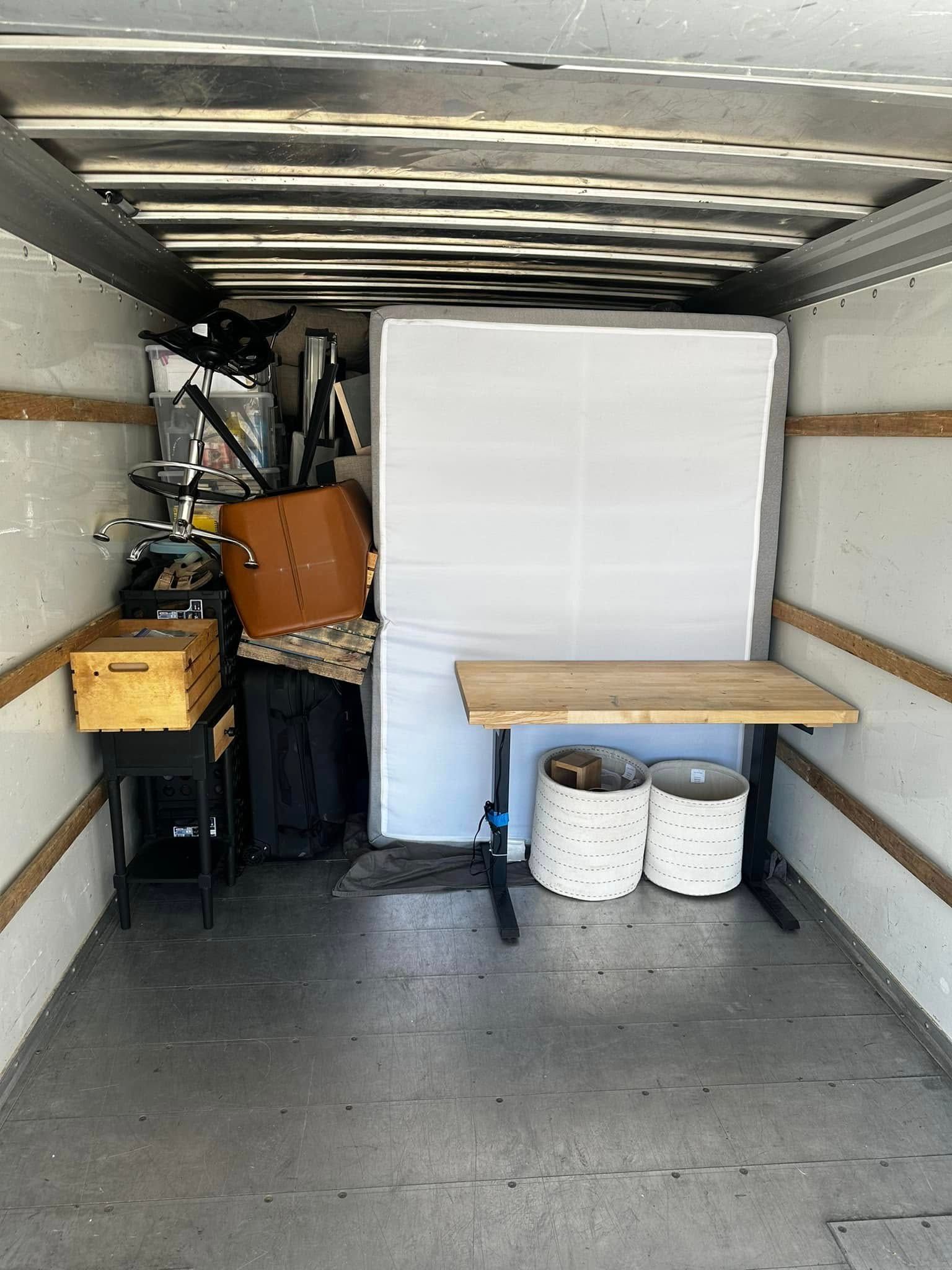 Interior of a moving truck with furniture, boxes, and other items. A mattress is on the back wall.