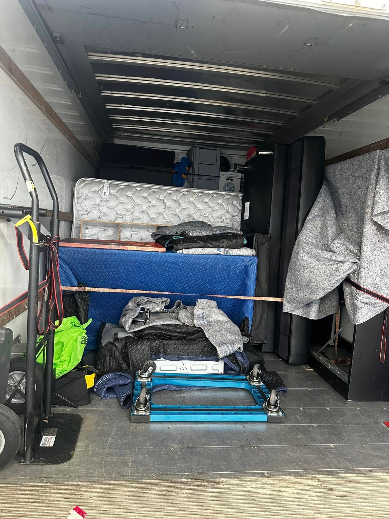 Inside of a truck filled with furniture and boxes. A hand truck is on the left.