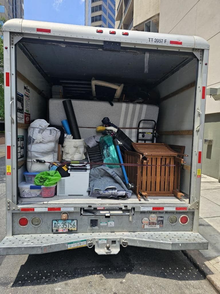 Open back of a moving truck filled with furniture, boxes, and miscellaneous items. Sunny day.