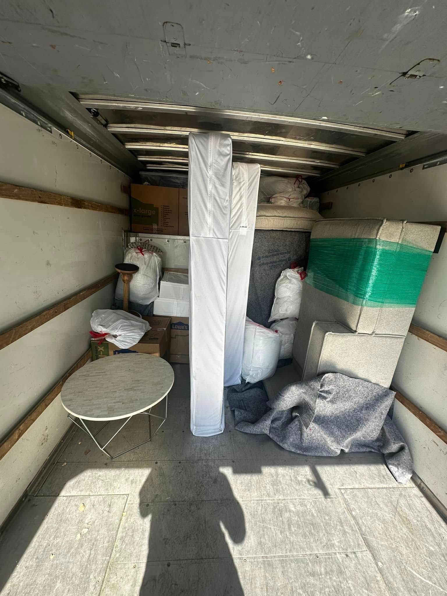 Inside a moving truck: furniture, boxes, and wrapped items are loaded for transport.