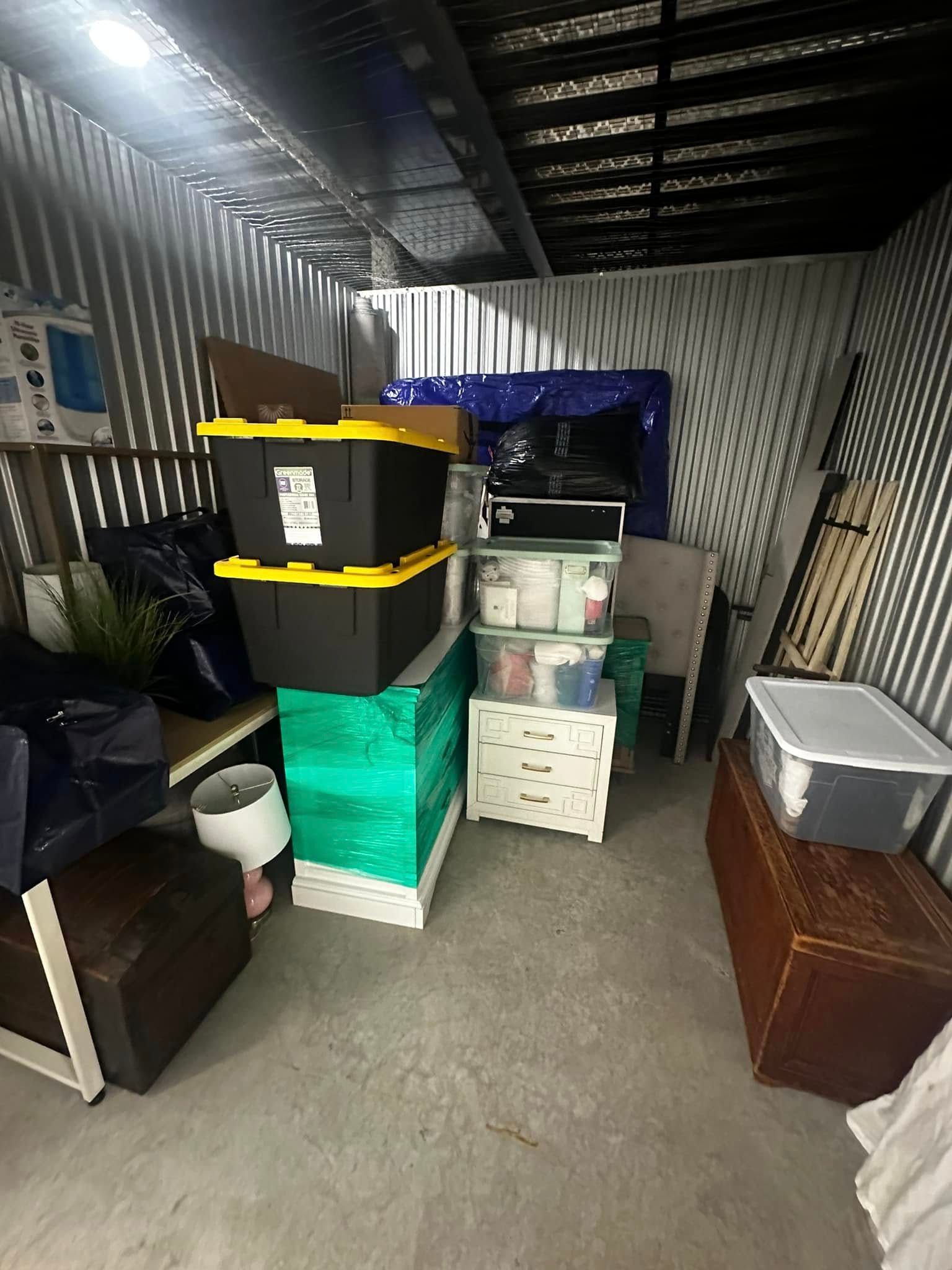 Storage unit packed with boxes, furniture, and various items, with metal walls and ceiling.