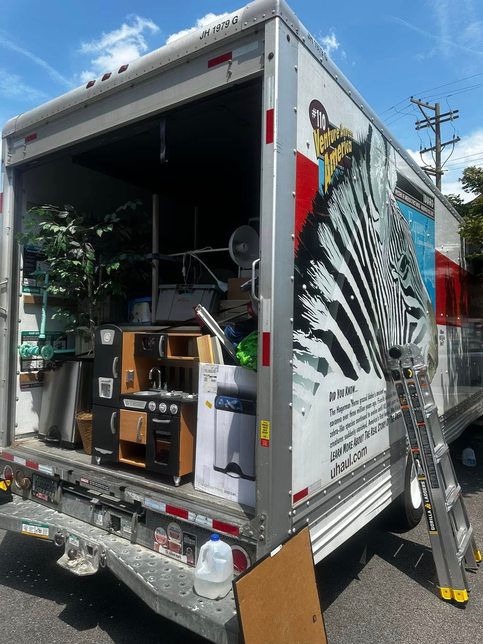 A moving truck loaded with furniture, boxes, and household items, partially open with a zebra graphic.