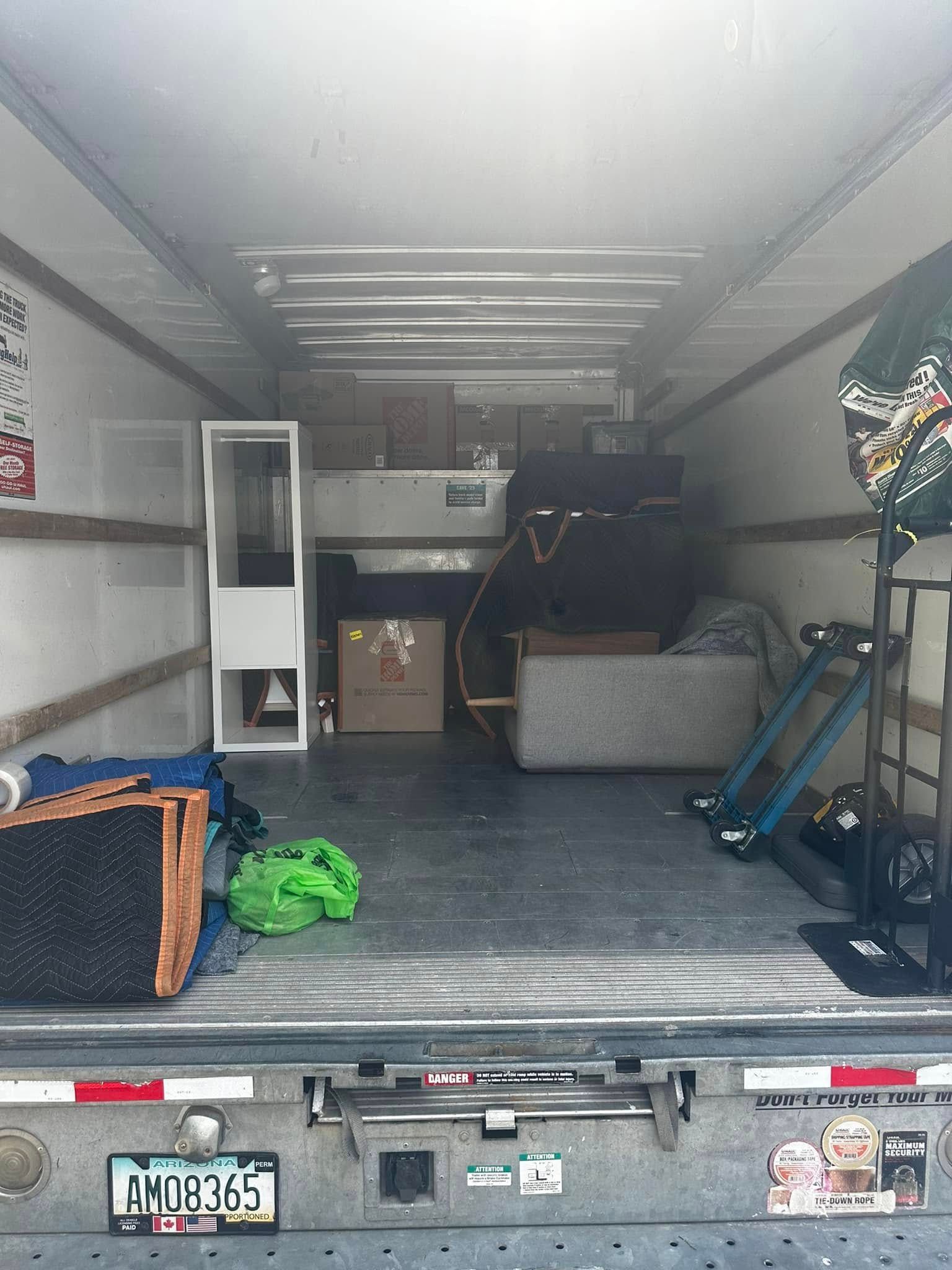 Inside a moving truck filled with furniture and boxes; a white cabinet is on the left.