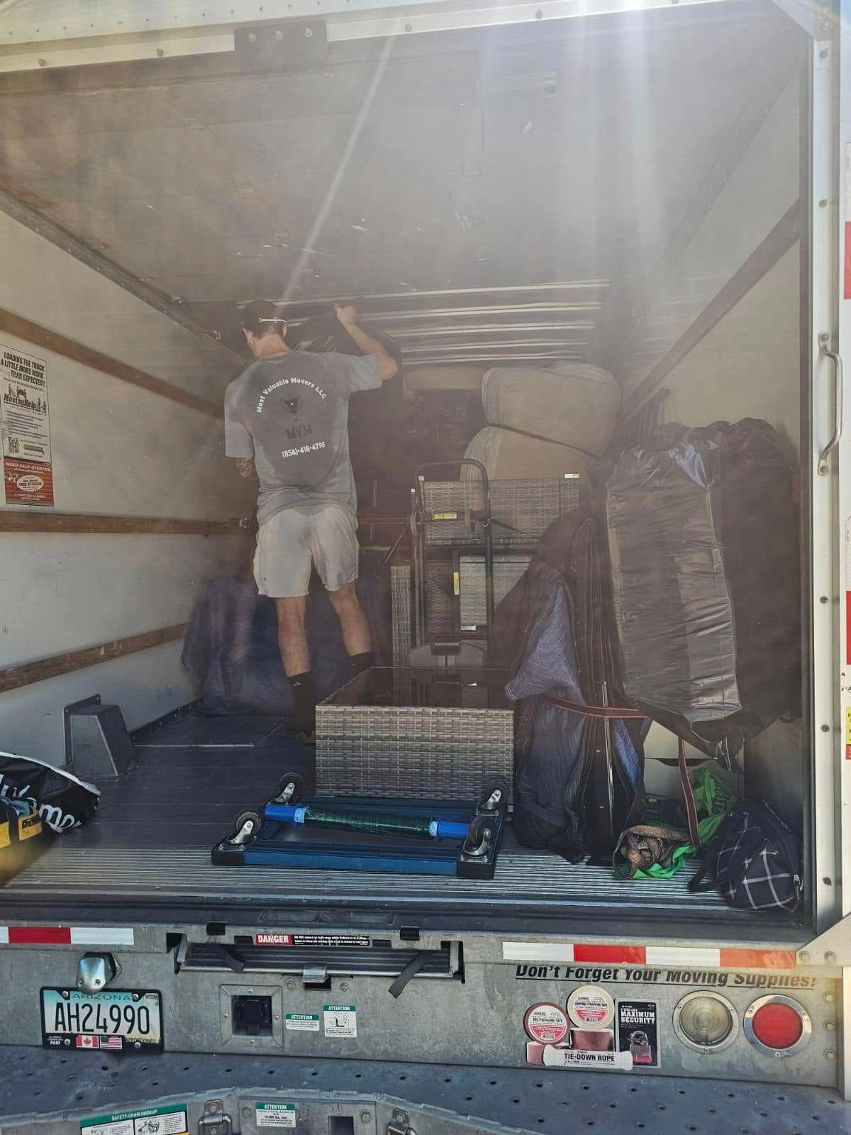 Man inside a moving truck, loading items. Sunlight streams in.