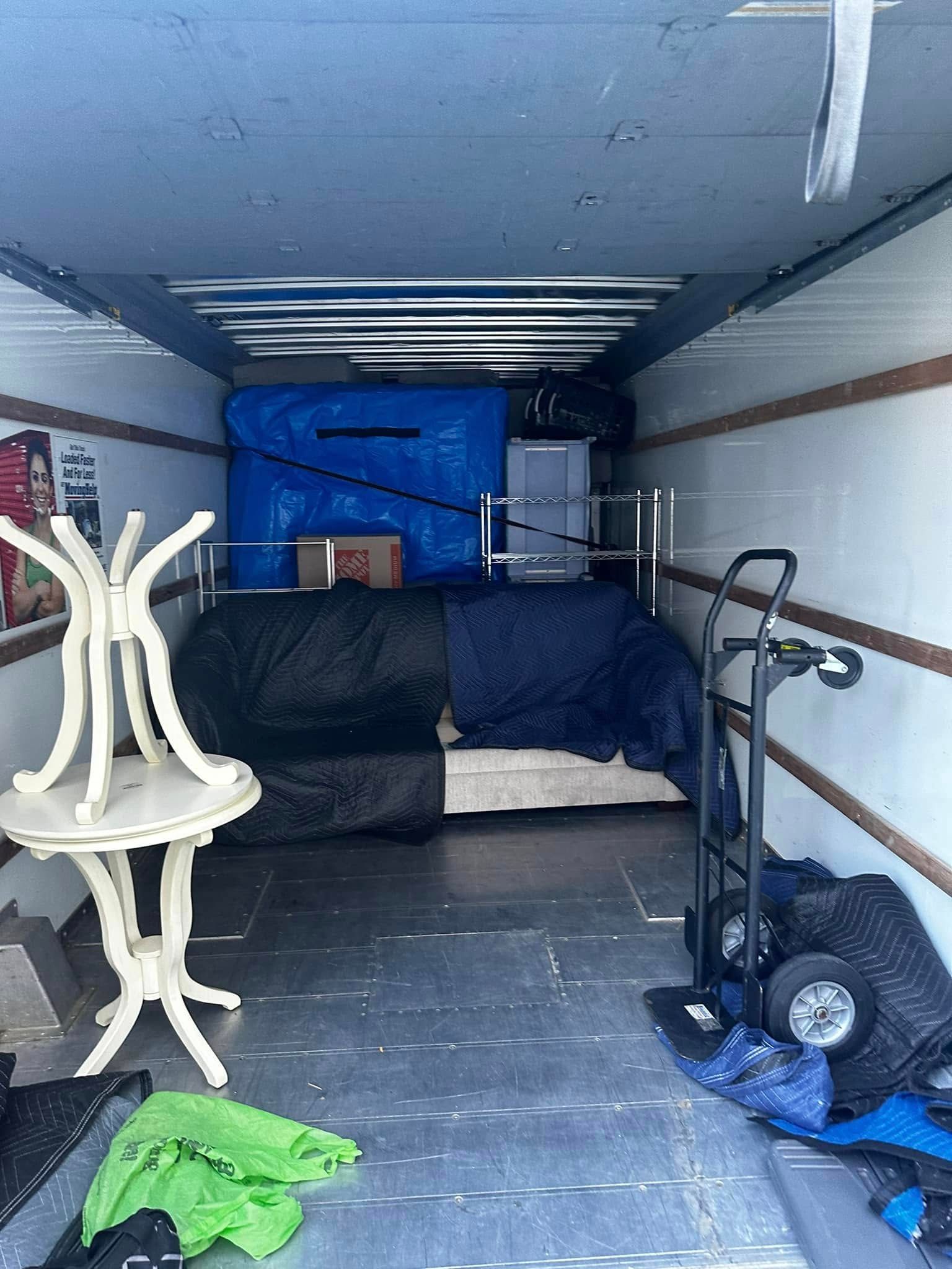 A moving truck interior with furniture: table, sofa, boxes, dolly.