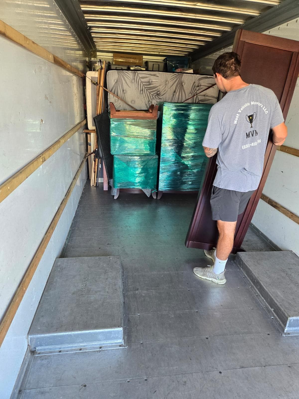 Man loading furniture into a moving truck. Interior view shows wrapped items and mattress.