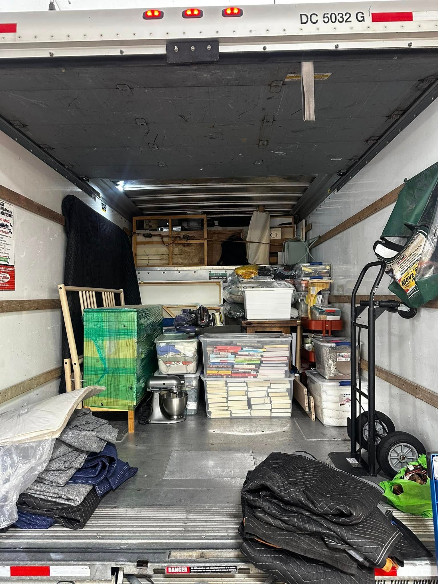 Inside of a moving truck packed with boxes, furniture, and miscellaneous items.