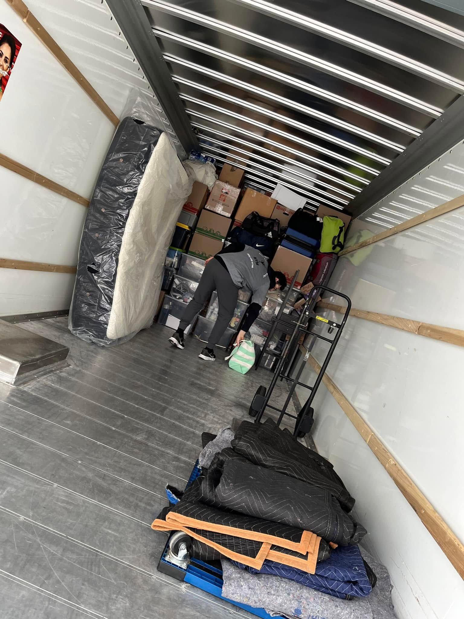 Person inside a moving truck packing boxes and items. Mattress and various belongings are also visible.