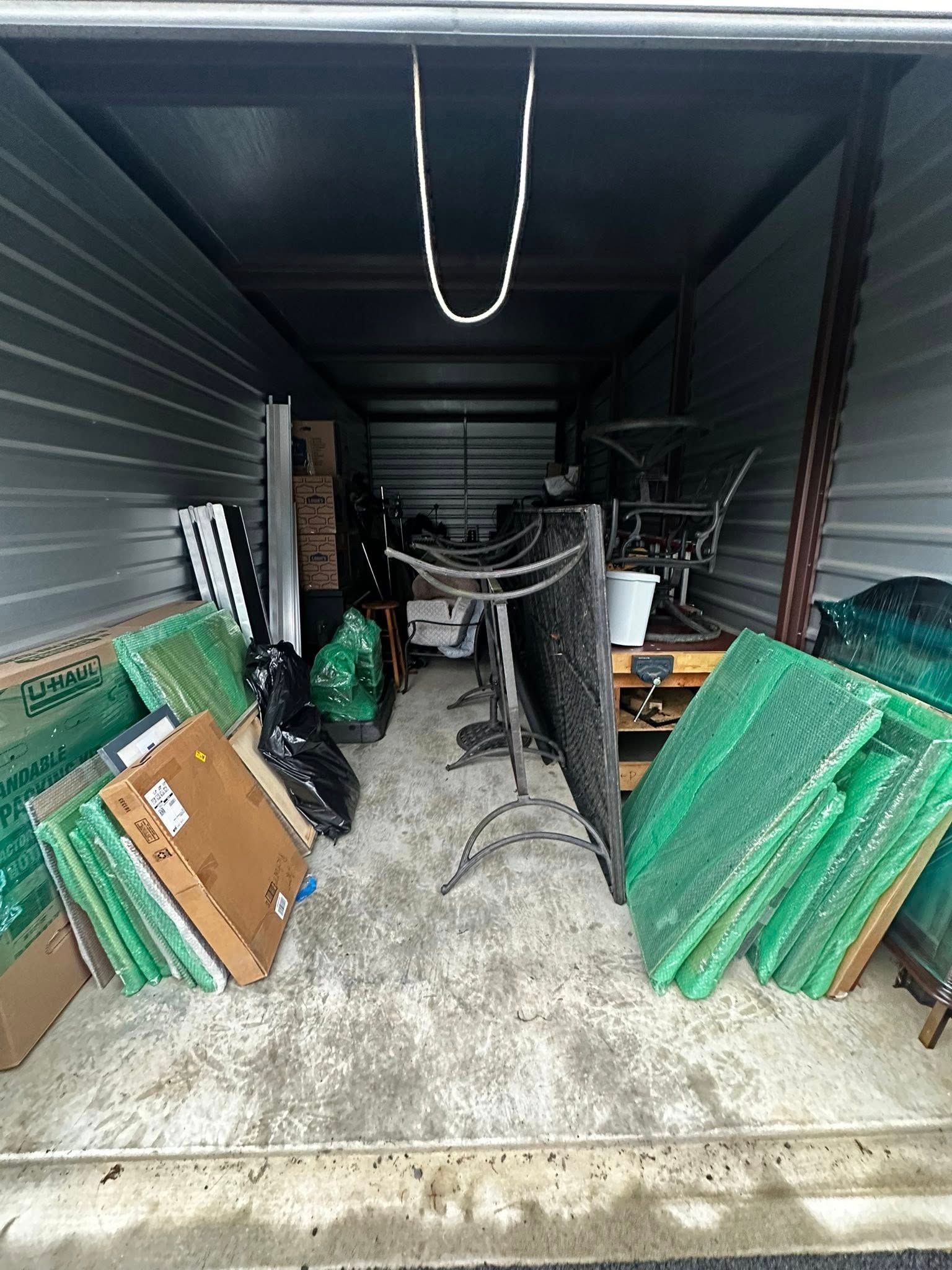 Storage unit packed with various items, including green wire fencing, boxes, and furniture.