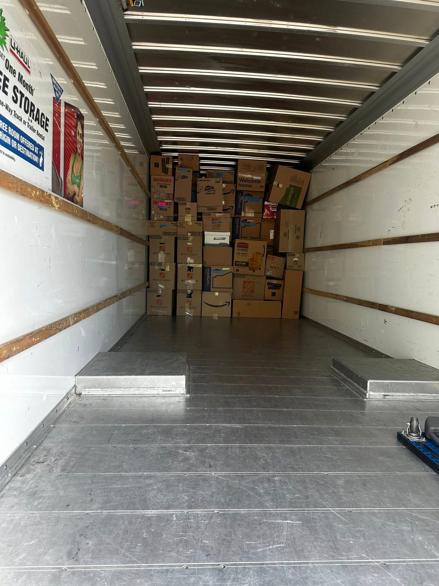 Inside a truck, boxes piled high. Metal floor and white walls. Sunlight streams through the roof.