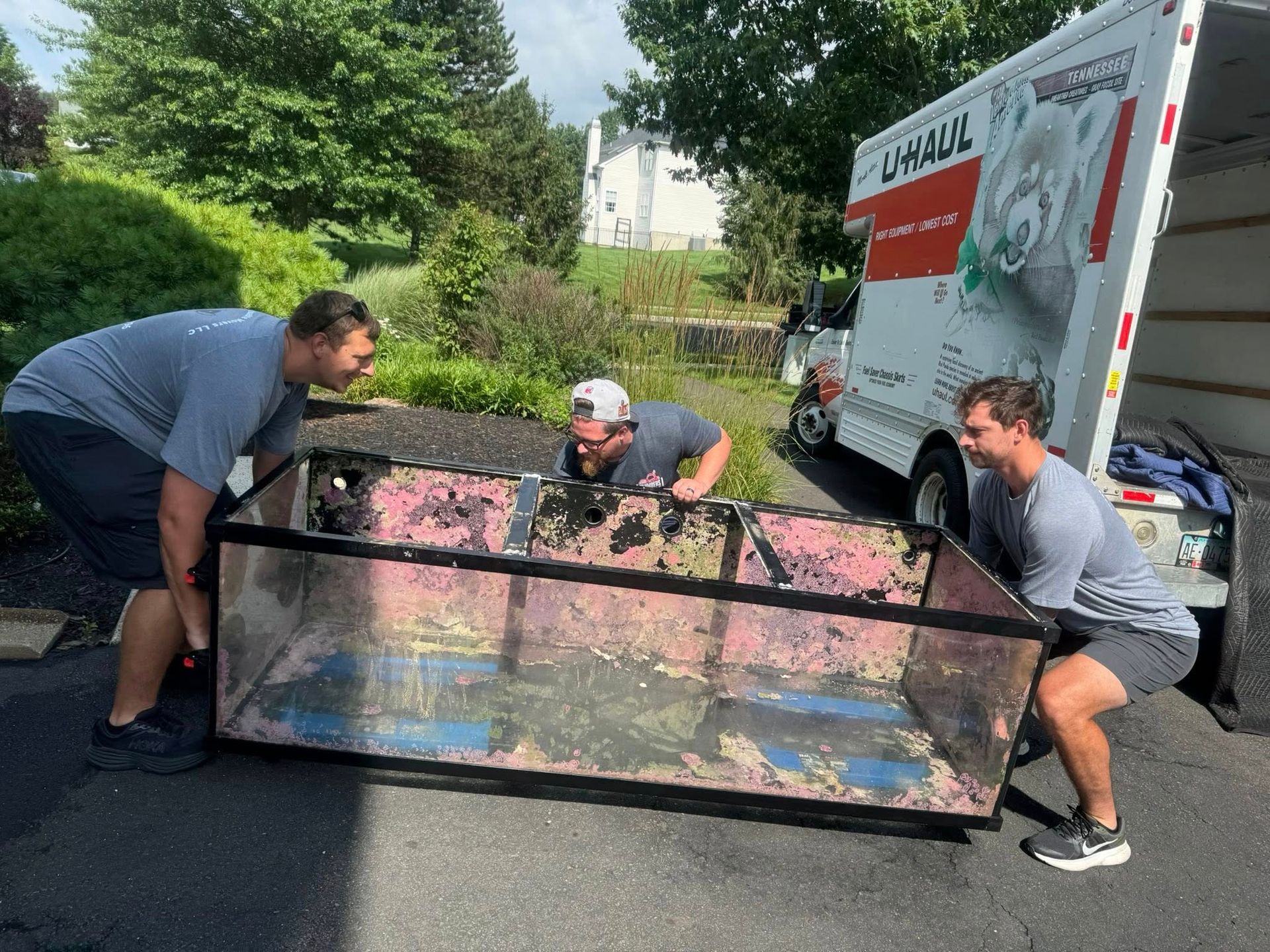 Three men loading a large, colorful bin into a U-Haul truck on a paved driveway.