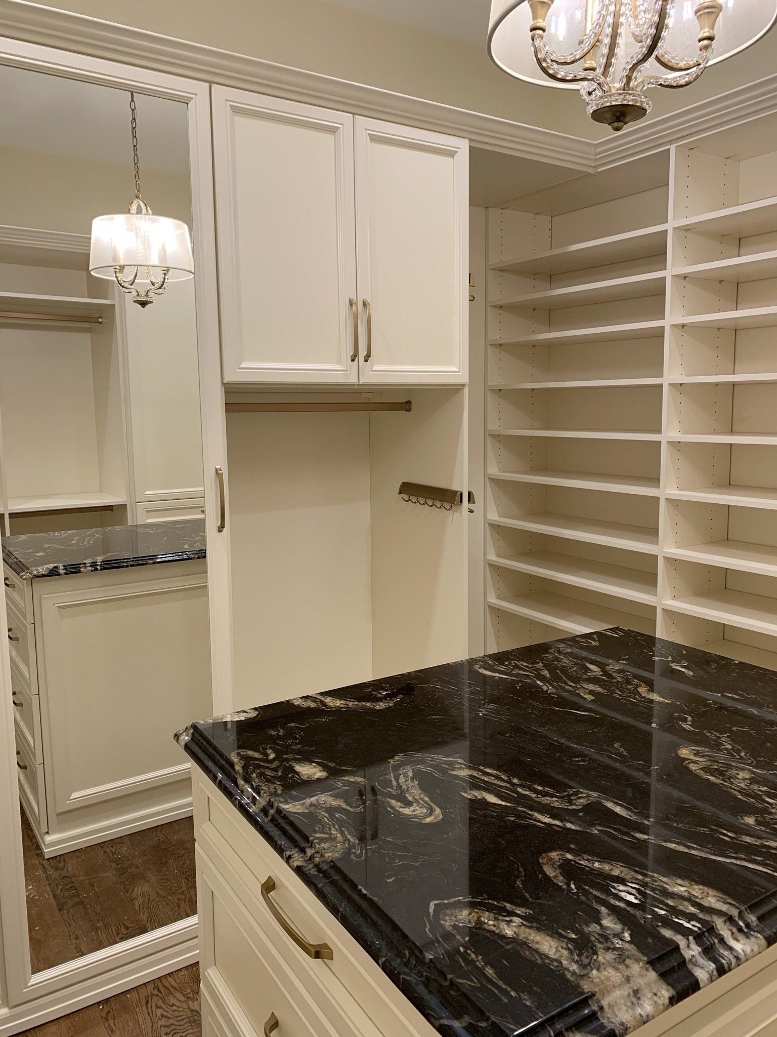 A walk in closet with a black granite counter top and white cabinets.