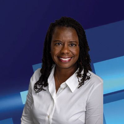 Woman with dreadlocks, smiling, wearing a white button-down shirt, against a blue background.