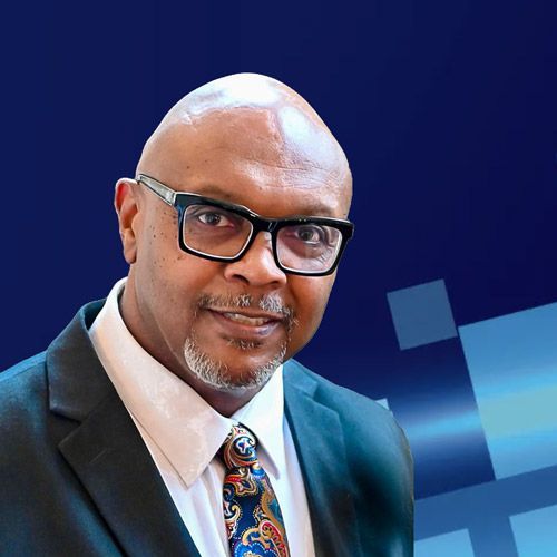 A smiling person wears glasses, a suit, and a colorful patterned tie against a dark blue background with digital squares.