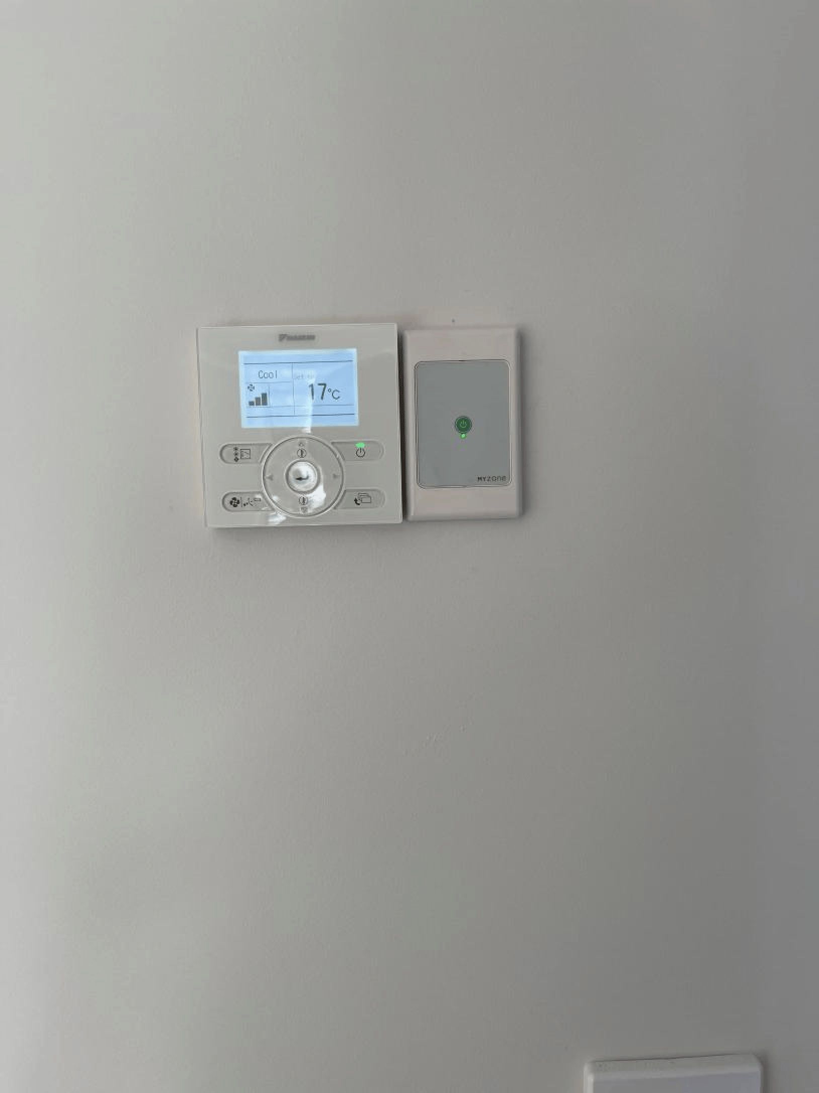 A white thermostat is hanging on a white wall.
