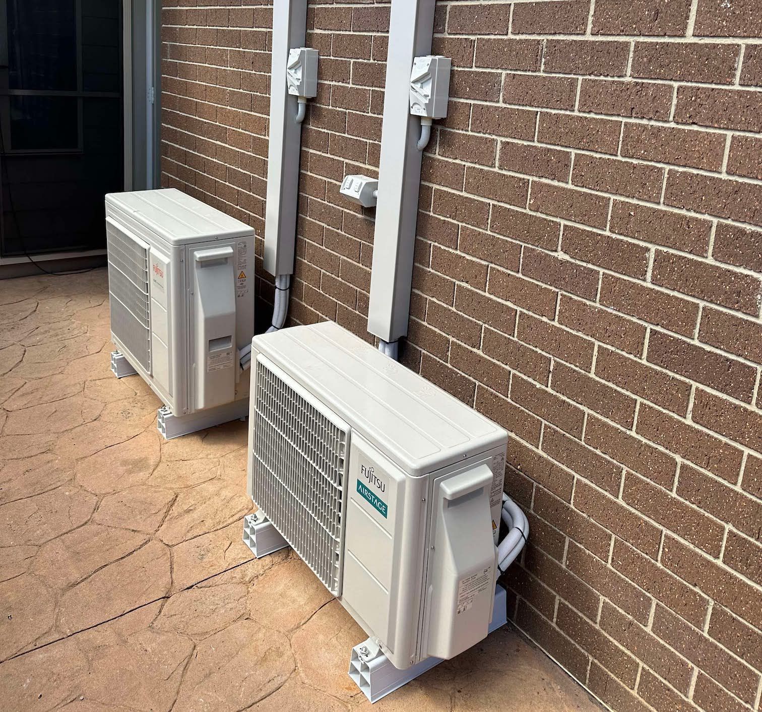 Two air conditioners are sitting on the side of a brick building.