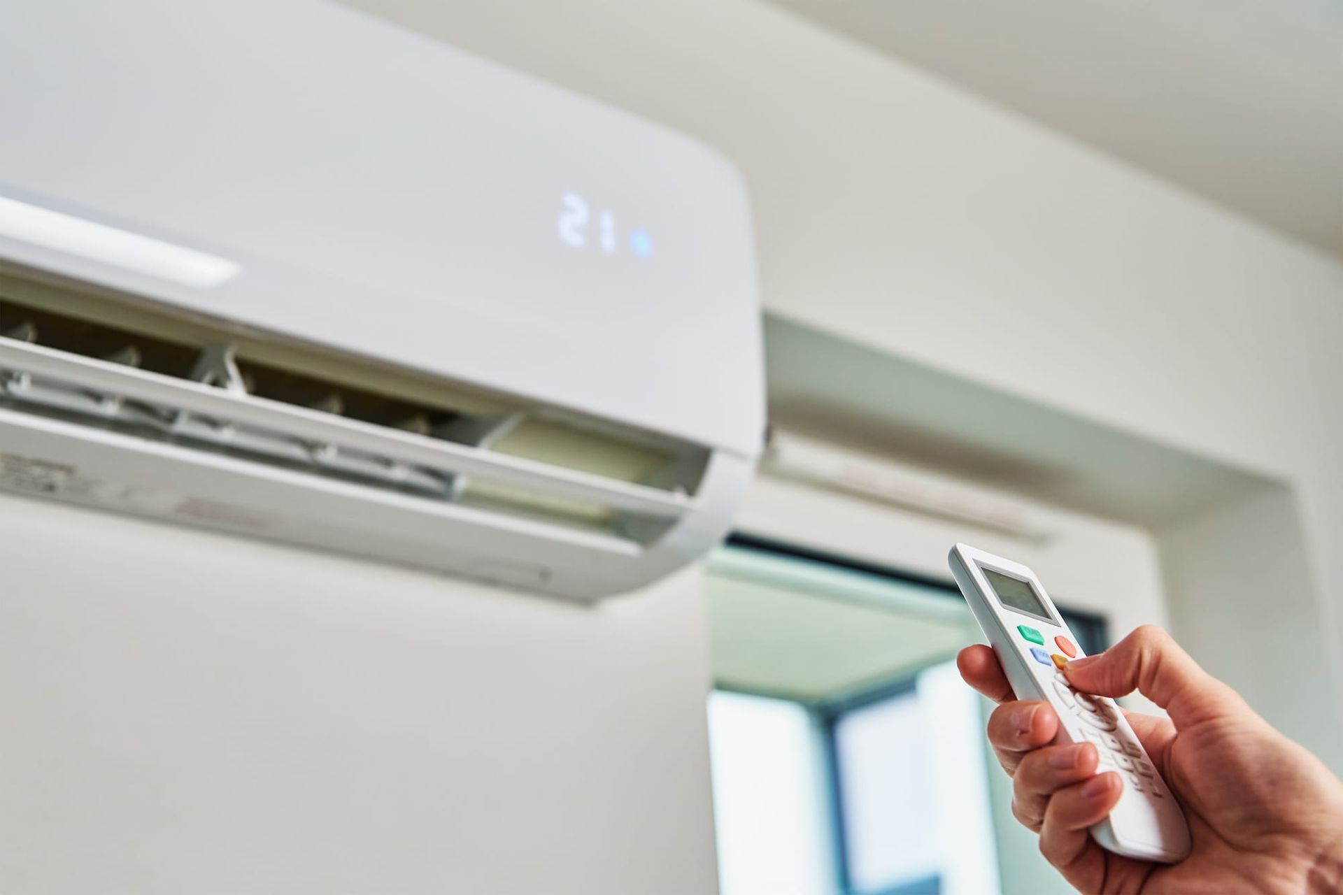 A person is holding a remote control in front of an air conditioner.