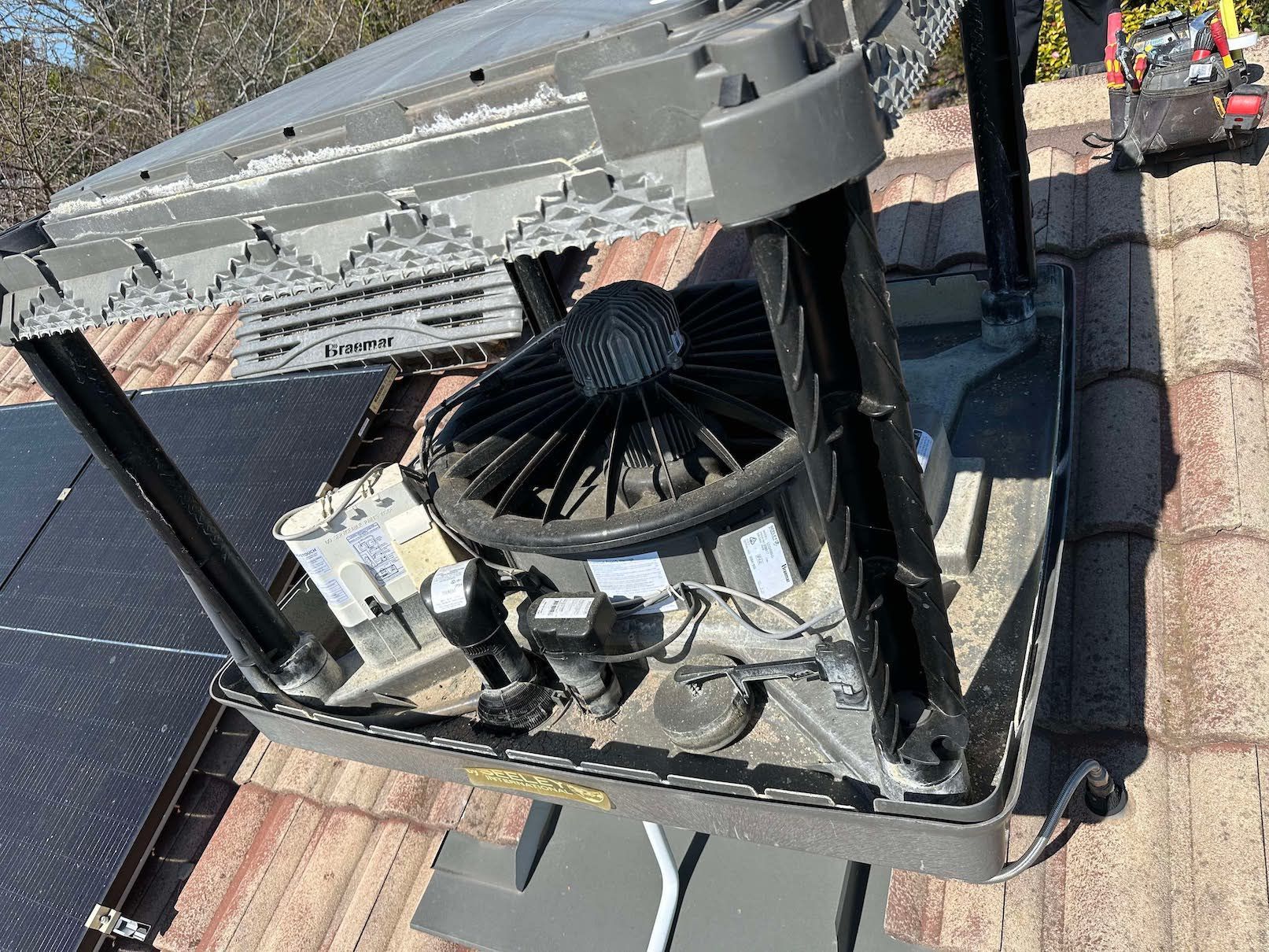A fan is sitting on top of a roof next to solar panels.