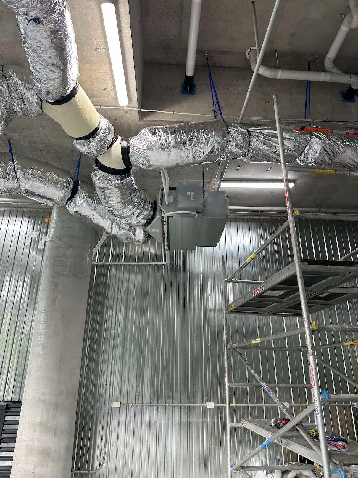  system installed in a ceiling with silver ductwork, lights, and a scaffolding in a construction zone.