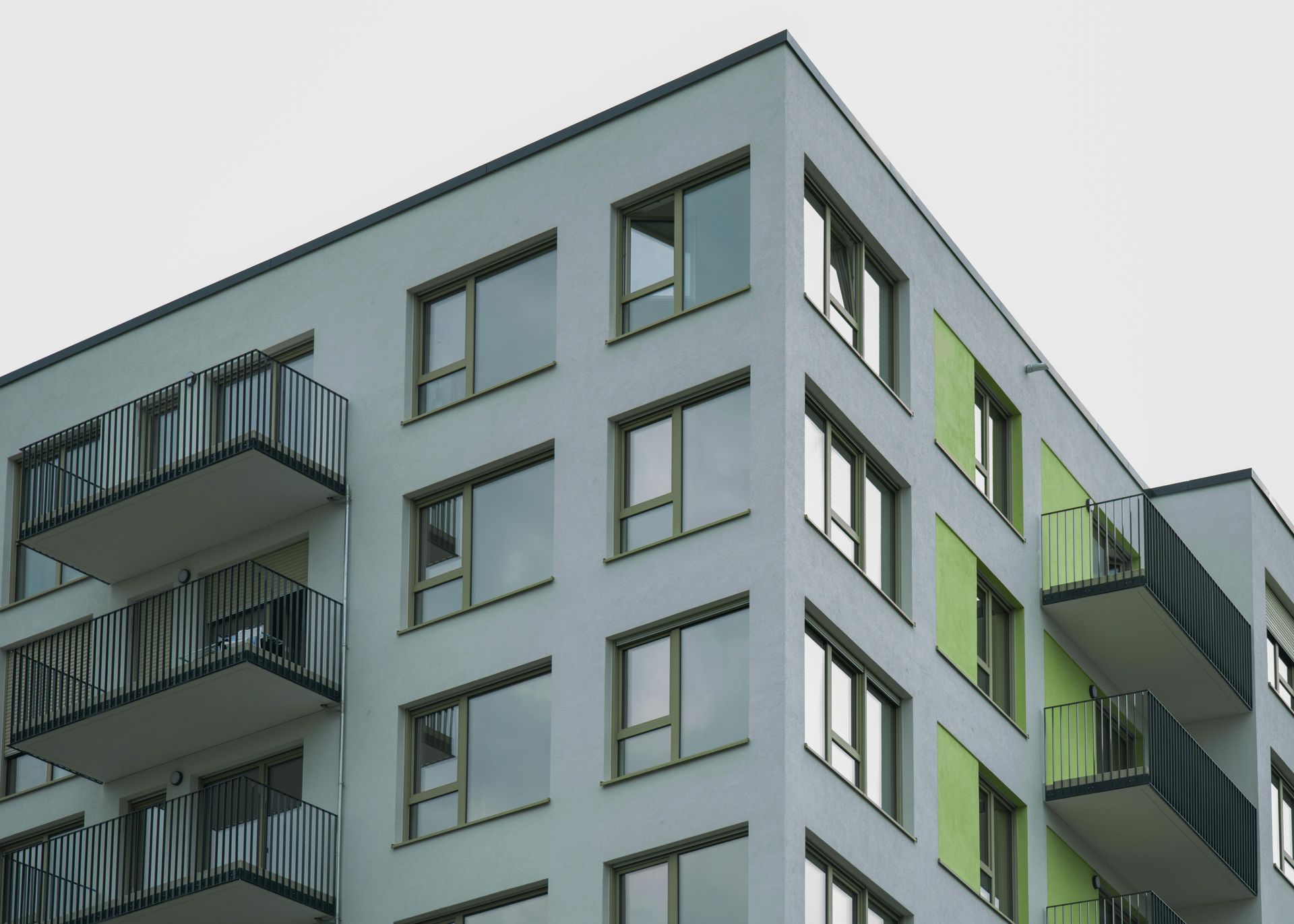 A corner view of a modern light-gray apartment building featuring recessed balconies, large windows, and lime green panels.