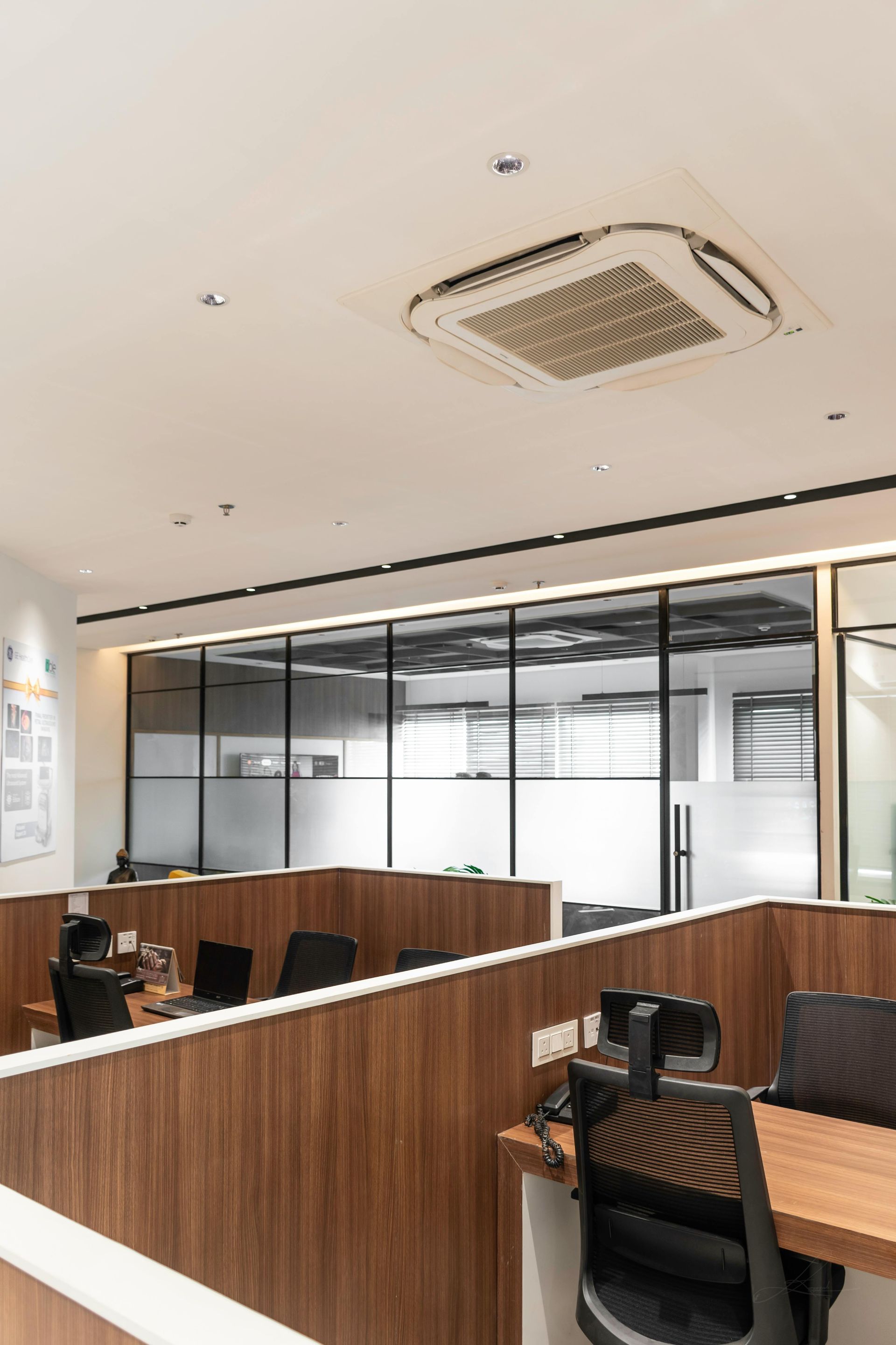 Modern office with wood desks, glass partitions, and ceiling air conditioner in a bright workspace