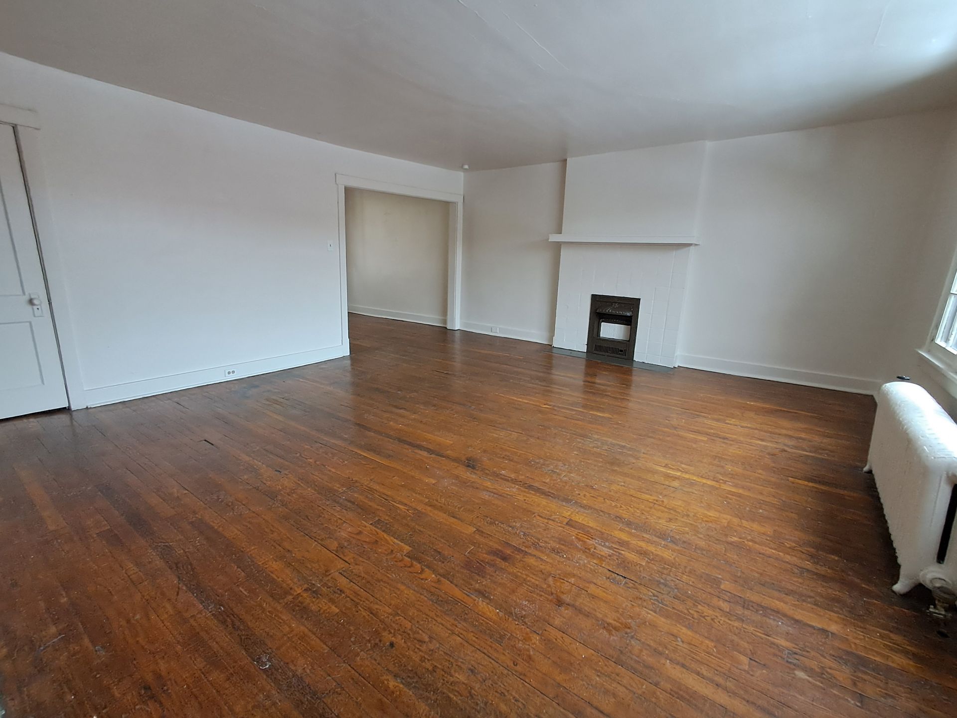Empty living room with hardwood floors, fireplace, and white walls.