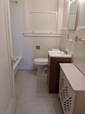 Bathroom with white walls, hexagon tile floor, toilet, vanity, and window.