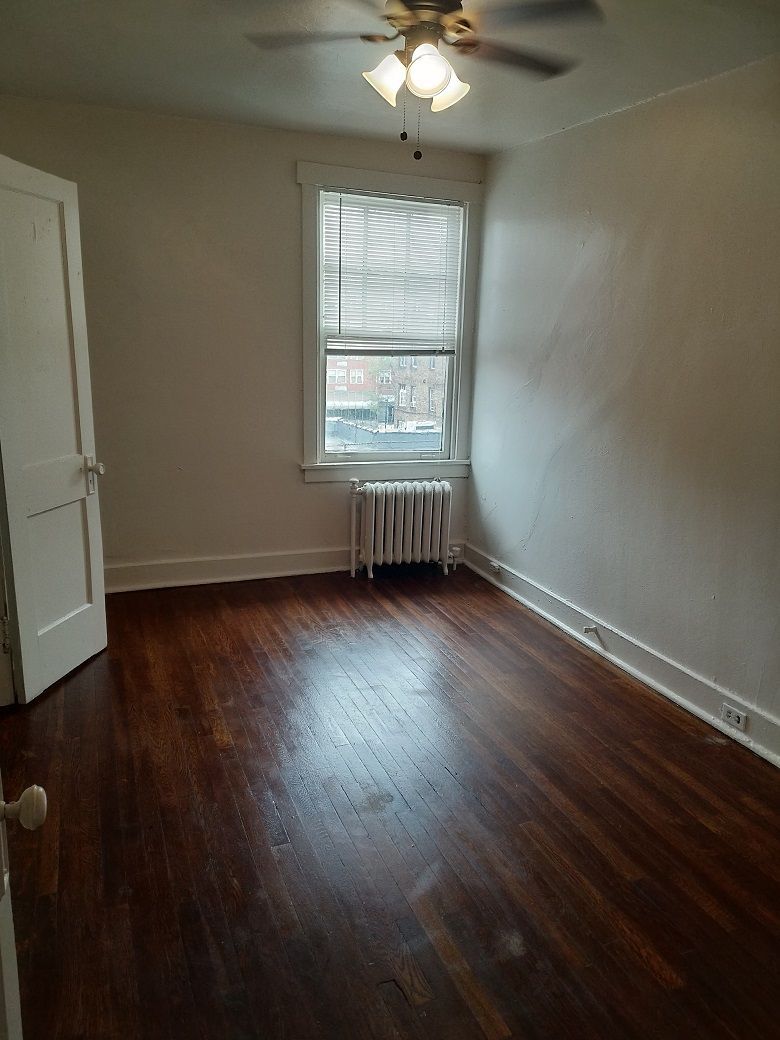Empty bedroom with dark wooden floors, a window, and a radiator.