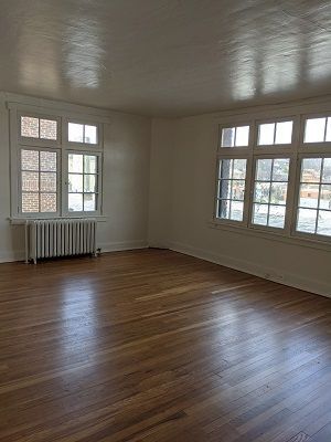 Empty room with hardwood floors, white walls, large windows, and a radiator.