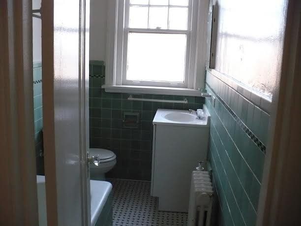 Bathroom with green tiled walls, white sink and toilet, and a window.