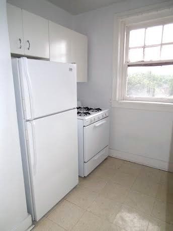 White kitchen with a refrigerator, stove, cabinets, and a window.