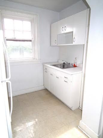 Small, white kitchen with sink, cabinets, and window.