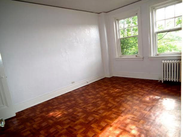Empty room with parquet flooring, white walls, two windows, and a radiator.