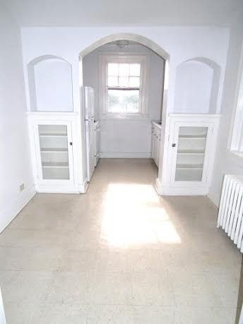 Kitchen with white cabinets, archway, refrigerator, and window. Beige carpet.