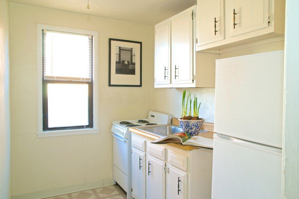 Small white kitchen with appliances, cabinets, a window, and a framed picture.