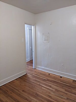 Empty room with hardwood floors, white walls, doorway leading to another room.