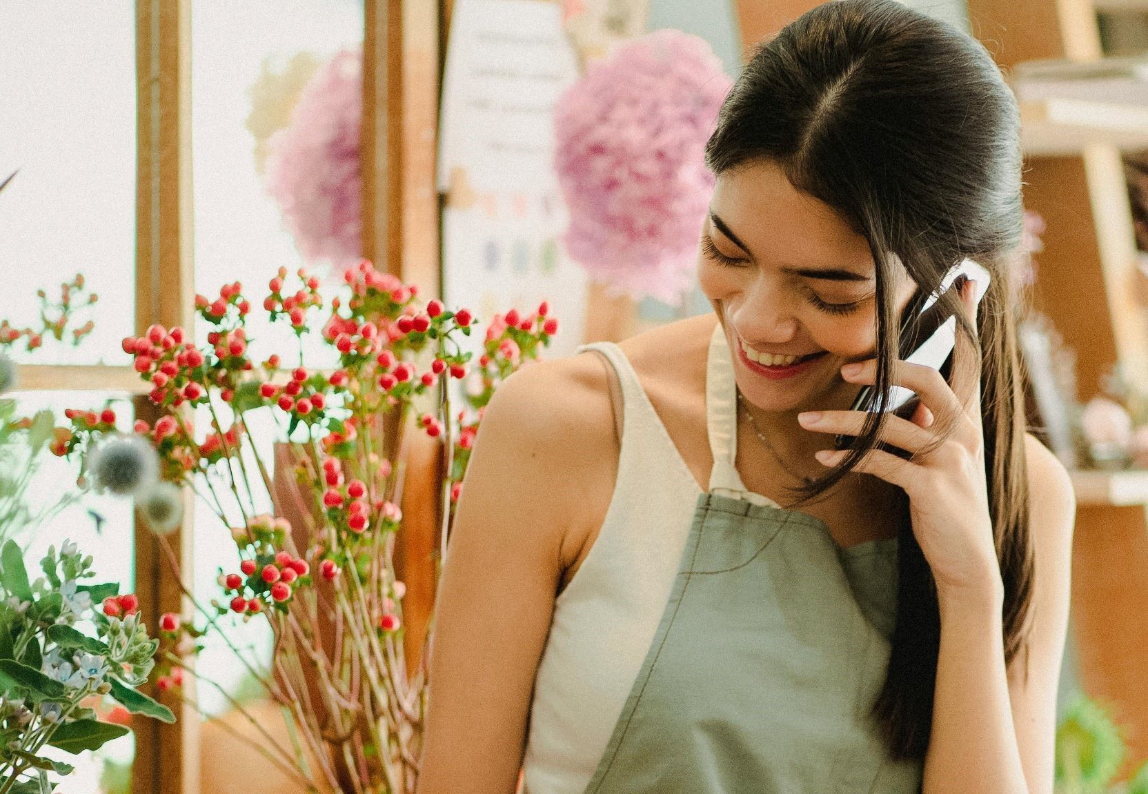 A female wearing an apron with flowers on her background is writing something on a paper.