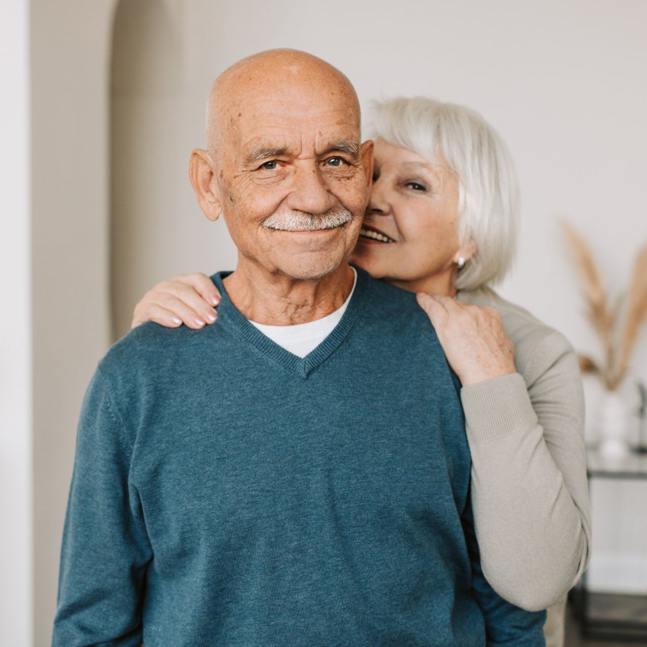 a woman is hugging an older man in a blue sweater .